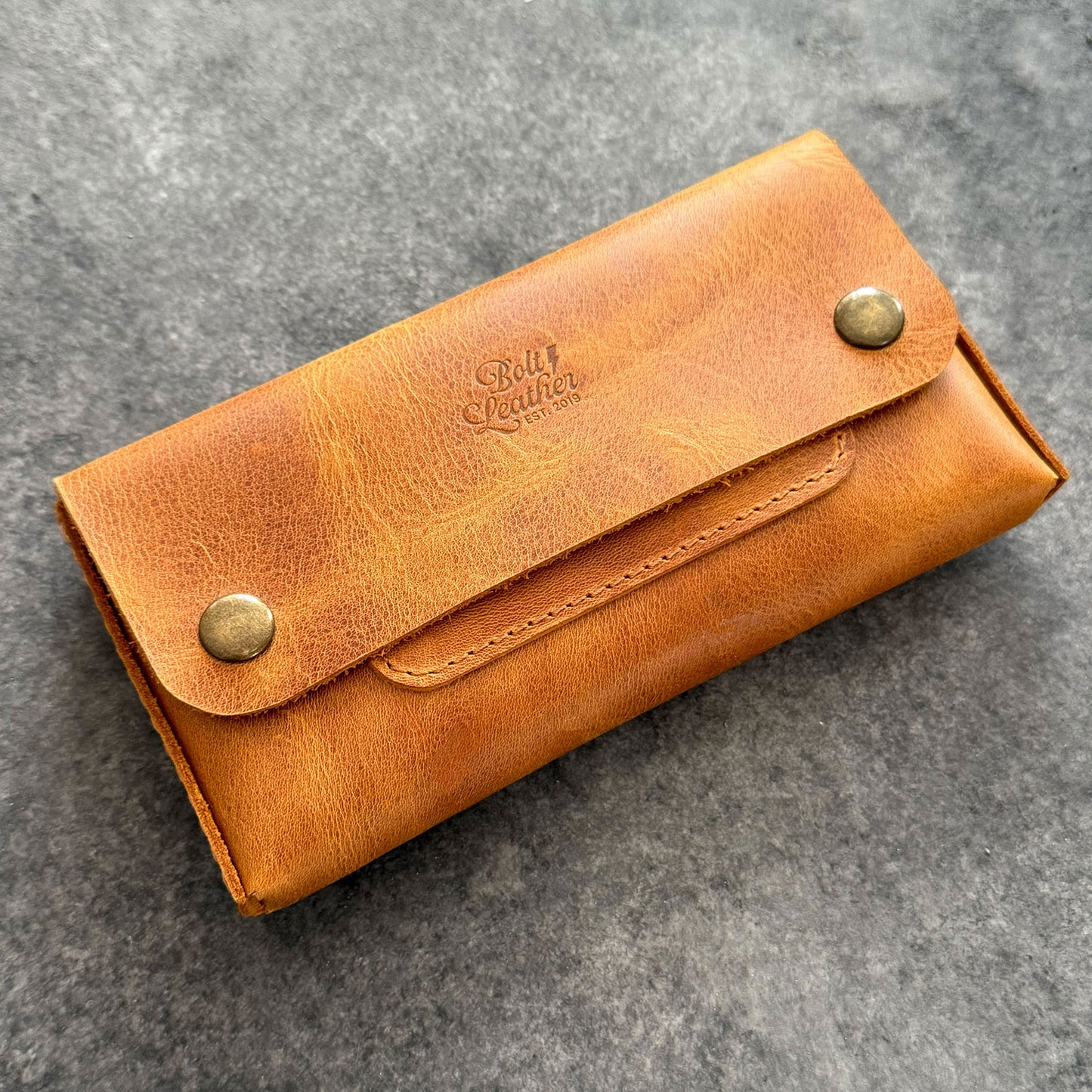 El yapımı, camel renkli deri tütün kesesi. Kişisel isim baskısı seçeneğiyle özel bir hediye arayanlar için ideal. Bolt Leather kalitesiyle doğal deri dokusu ve el işçiliği.