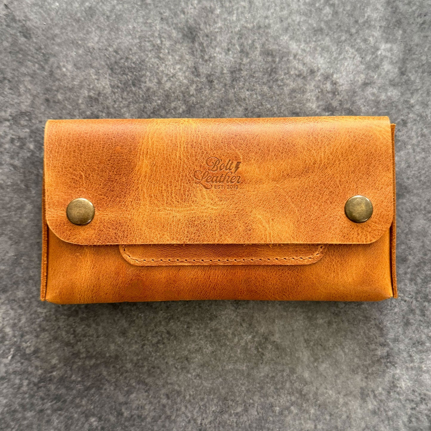 El yapımı, camel renkli deri tütün kesesi. Kişisel isim baskısı seçeneğiyle özel bir hediye arayanlar için ideal. Bolt Leather kalitesiyle doğal deri dokusu ve el işçiliği.