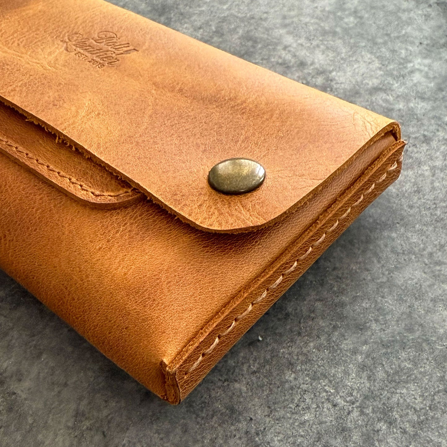 El yapımı, camel renkli deri tütün kesesi. Kişisel isim baskısı seçeneğiyle özel bir hediye arayanlar için ideal. Bolt Leather kalitesiyle doğal deri dokusu ve el işçiliği.