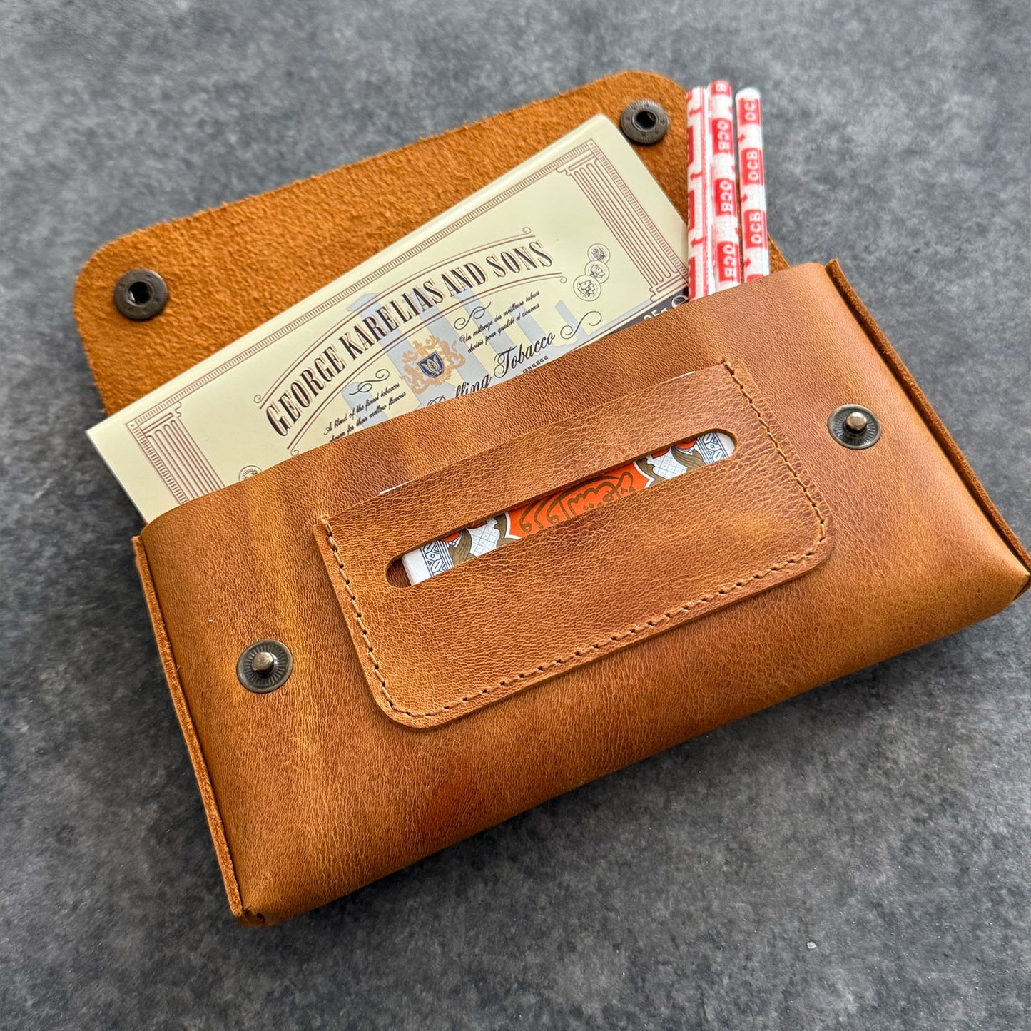 El yapımı, camel renkli deri tütün kesesi. Kişisel isim baskısı seçeneğiyle özel bir hediye arayanlar için ideal. Bolt Leather kalitesiyle doğal deri dokusu ve el işçiliği.