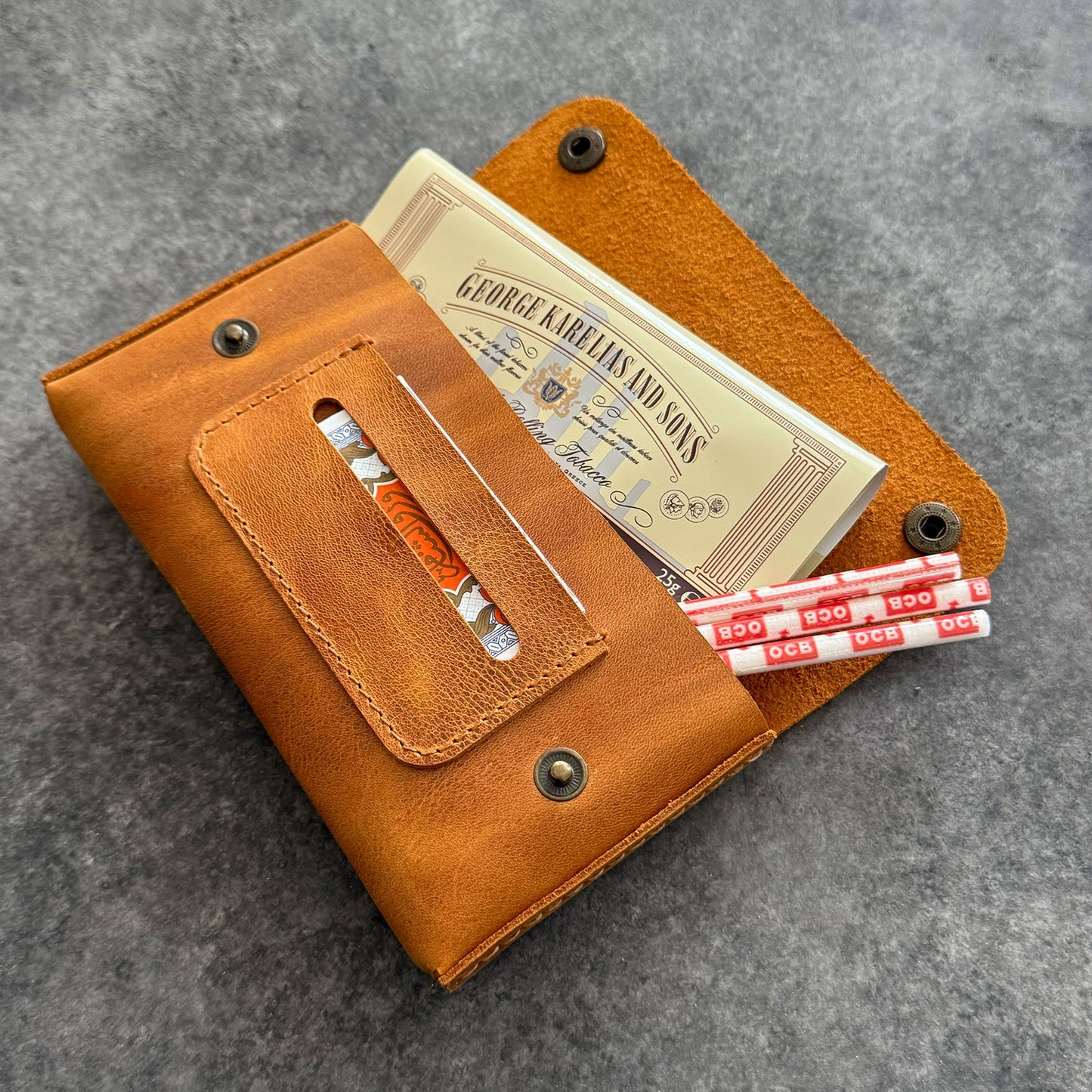 El yapımı, camel renkli deri tütün kesesi. Kişisel isim baskısı seçeneğiyle özel bir hediye arayanlar için ideal. Bolt Leather kalitesiyle doğal deri dokusu ve el işçiliği.
