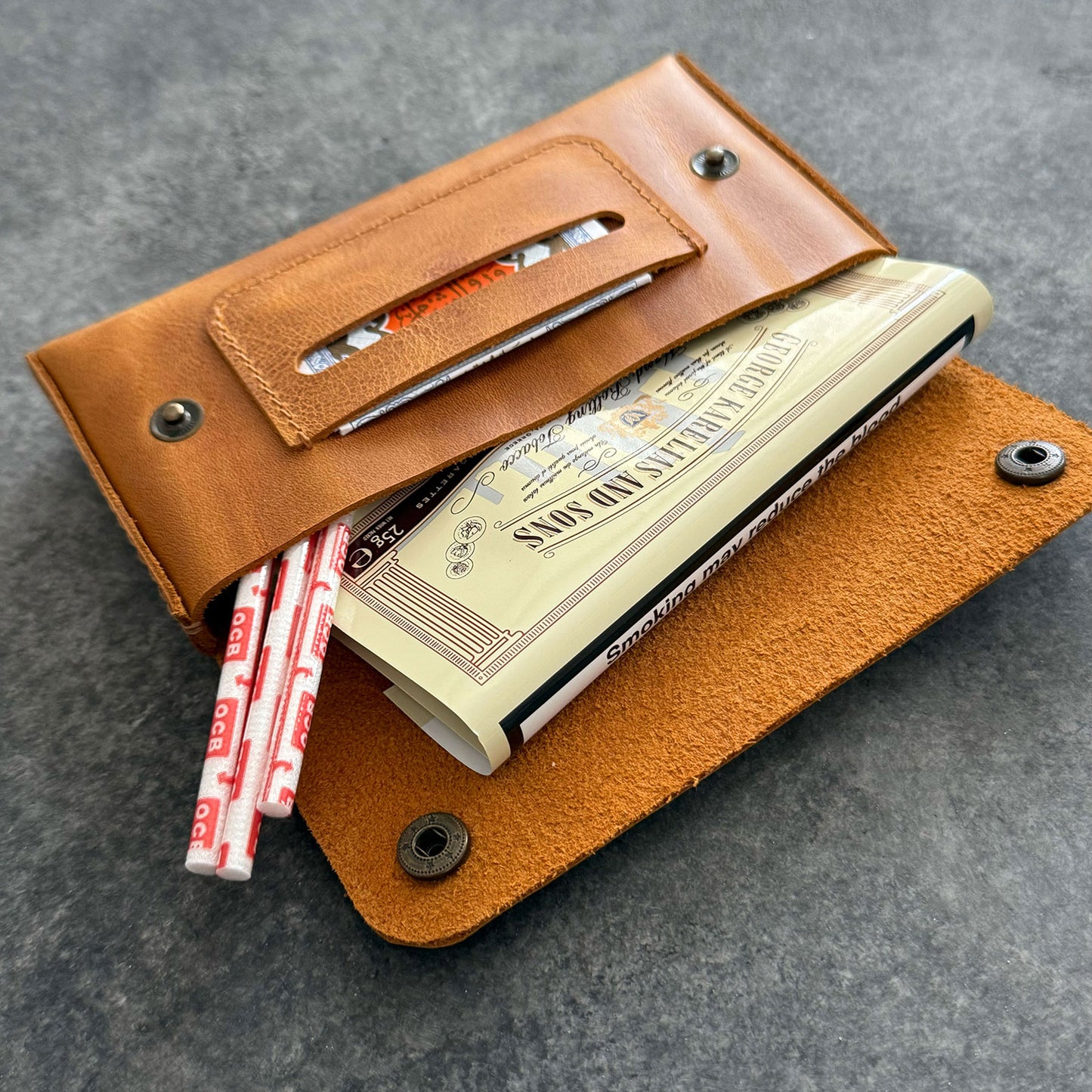 El yapımı, camel renkli deri tütün kesesi. Kişisel isim baskısı seçeneğiyle özel bir hediye arayanlar için ideal. Bolt Leather kalitesiyle doğal deri dokusu ve el işçiliği.