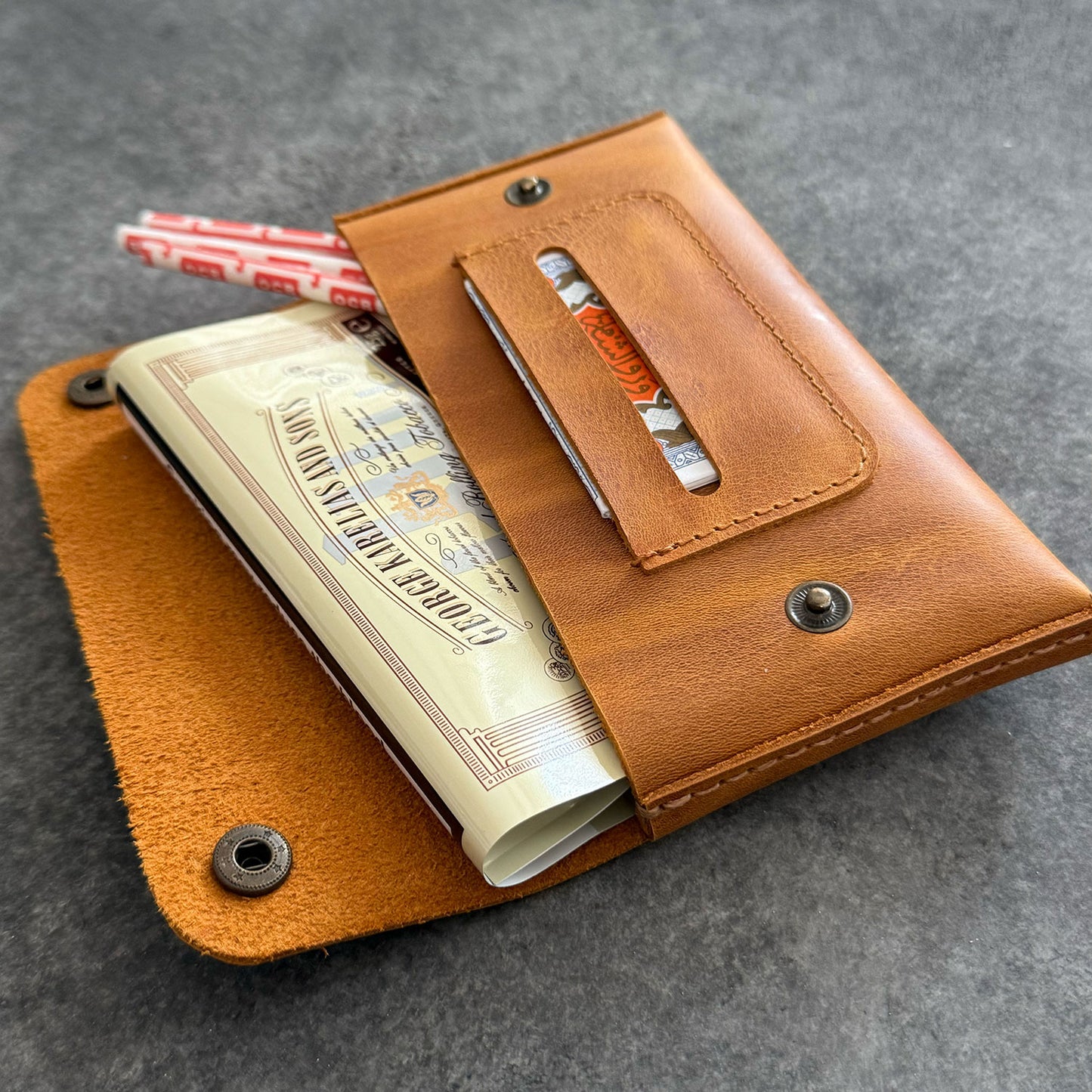 El yapımı, camel renkli deri tütün kesesi. Kişisel isim baskısı seçeneğiyle özel bir hediye arayanlar için ideal. Bolt Leather kalitesiyle doğal deri dokusu ve el işçiliği.