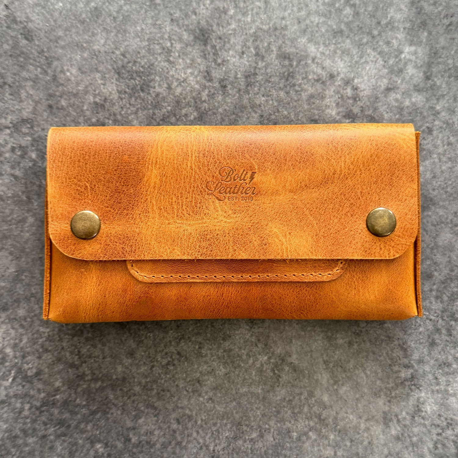 El yapımı, camel renkli deri tütün kesesi. Kişisel isim baskısı seçeneğiyle özel bir hediye arayanlar için ideal. Bolt Leather kalitesiyle doğal deri dokusu ve el işçiliği.